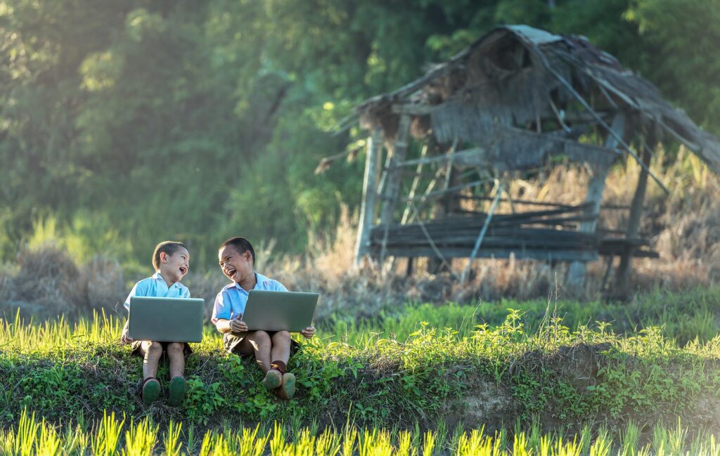 Dzieci siedzą na trawie z laptopami i śmieją się
